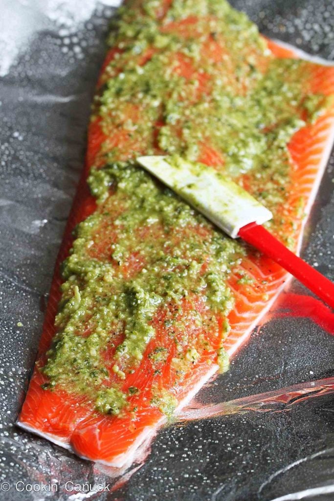 Spreading basil pesto on a salmon fillet.