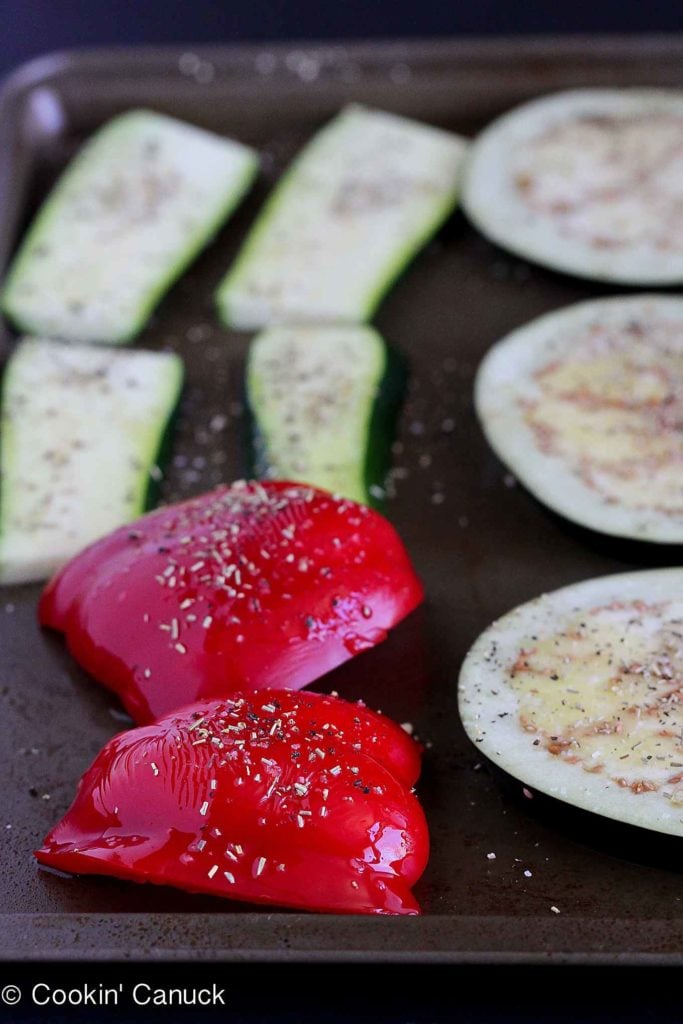 Eggplant, red bell peppers and zucchini slices on a baking sheet, brushed with olive oil.