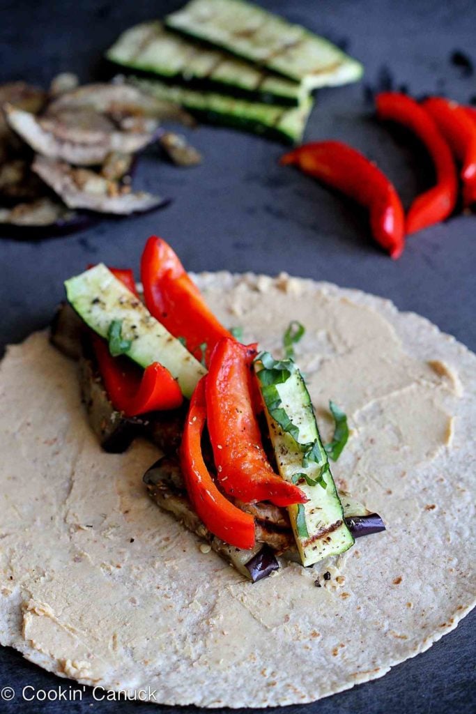 Sliced grilled vegetables on a whole wheat tortilla, layered with a spread of hummus.