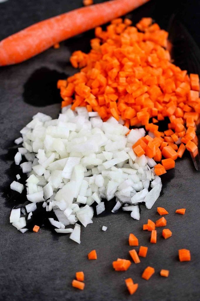 Chopped onions and carrots on a black cutting board.