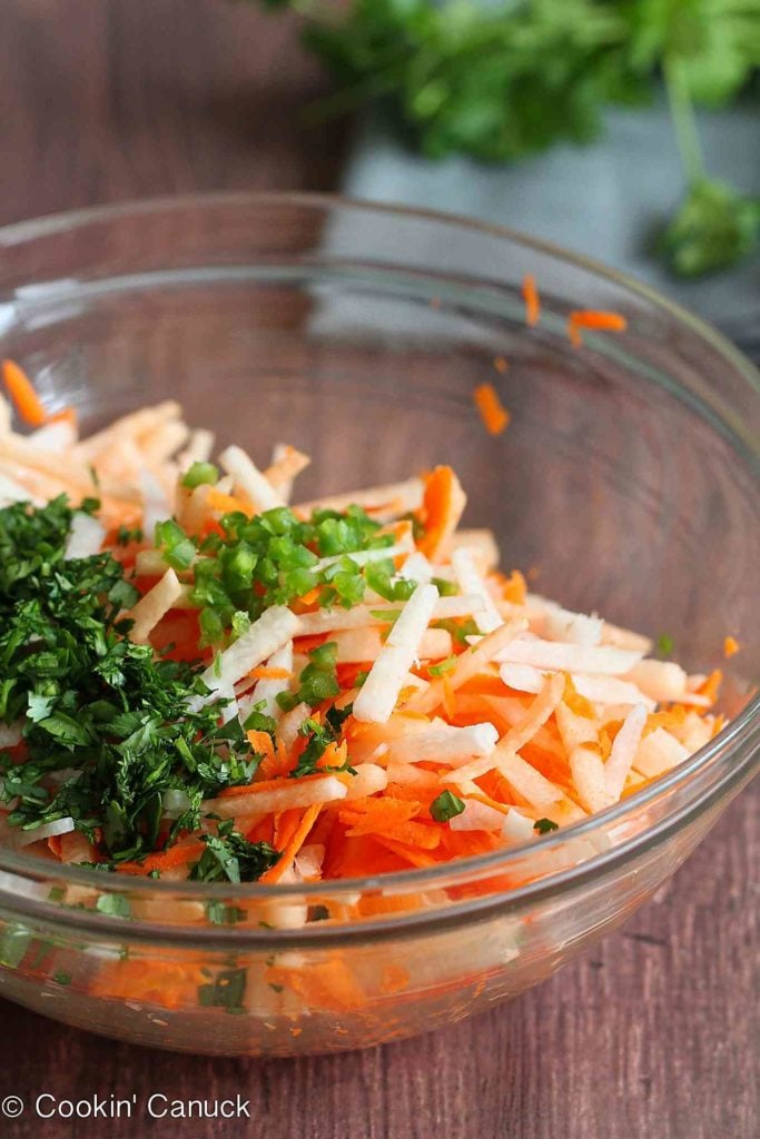 Sliced jicama, grated carrot and chopped cilantro in a large glass bowl.