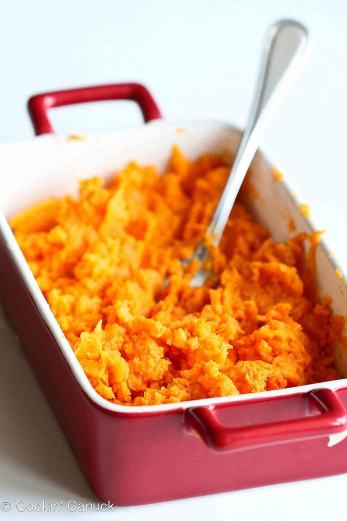 Mashed sweet potato in a small, red baking dish.