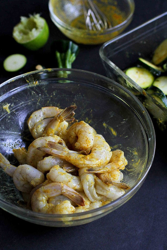 Raw shrimp, seasoned with curry powder and lime juice, in a glass bowl.