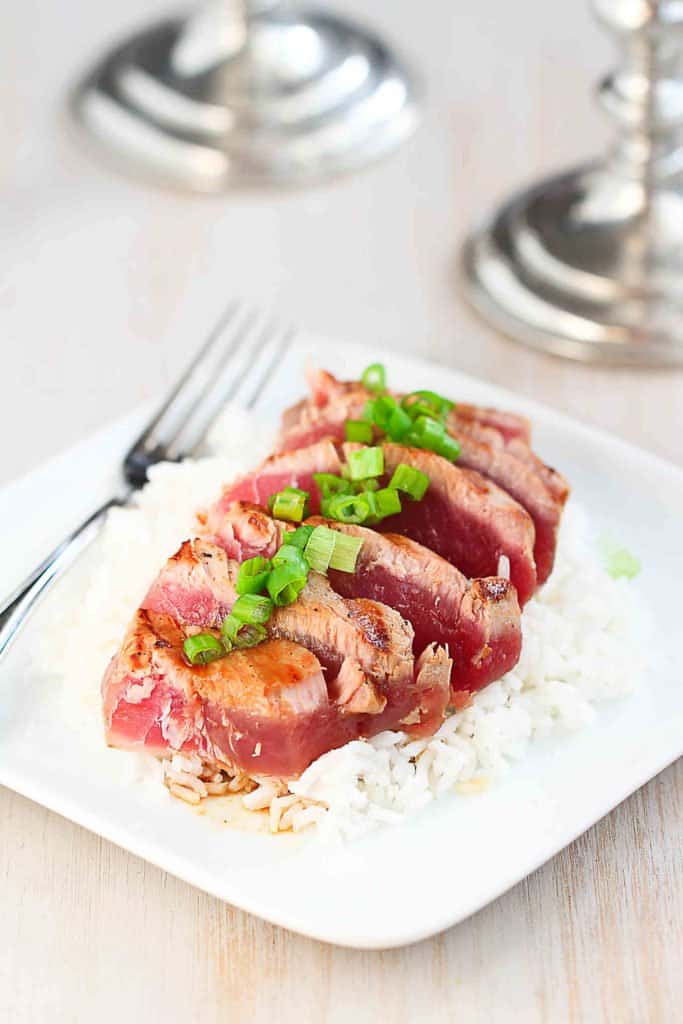 Sliced, seared ahi tuna topped with green onions, on a white plate.