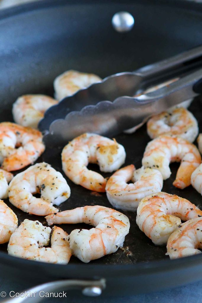 Seared shrimp in a nonstick skillet, with tongs.