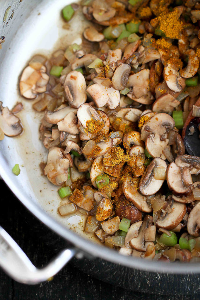 Sauteed mushroom and celery, along with curry powder, in a skillet.