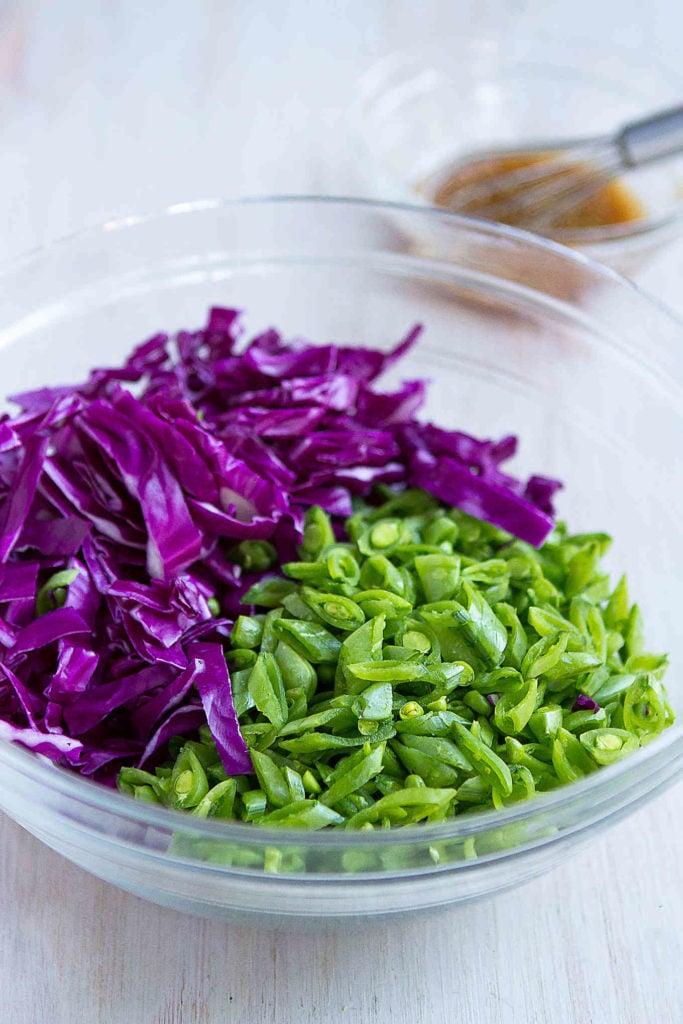 Sliced snap peas and red cabbage in a glass bowl, plus a bowl of hoisin dressing.