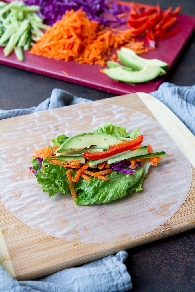 Vegetables layered on a spring roll wrapper, on a cutting board.