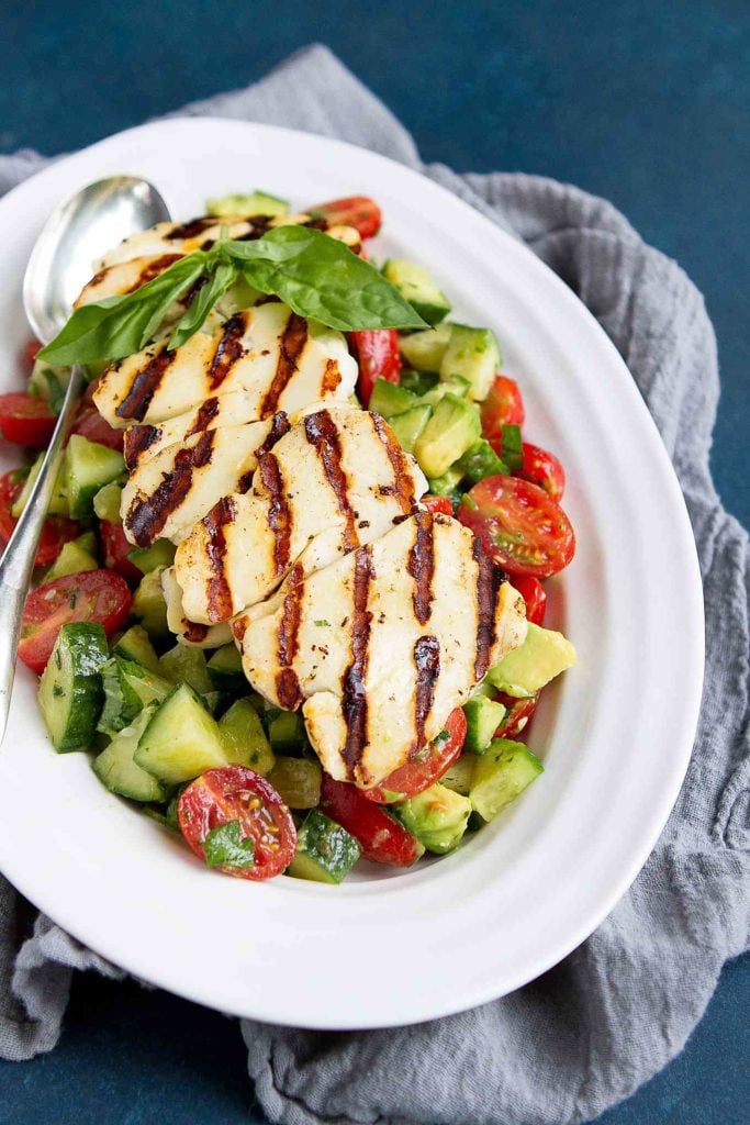 This cucumber, tomato and avocado salad recipe is made even better with some warm, grilled slices of halloumi cheese layered on top! 102 calories and 3 Weight Watchers Freestyle SP #grilling #wwfreestyle #healthysalads