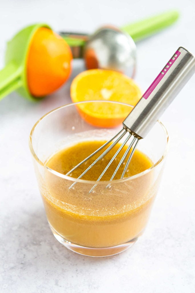 Orange and lemon vinaigrette in a glass with a whisk.
