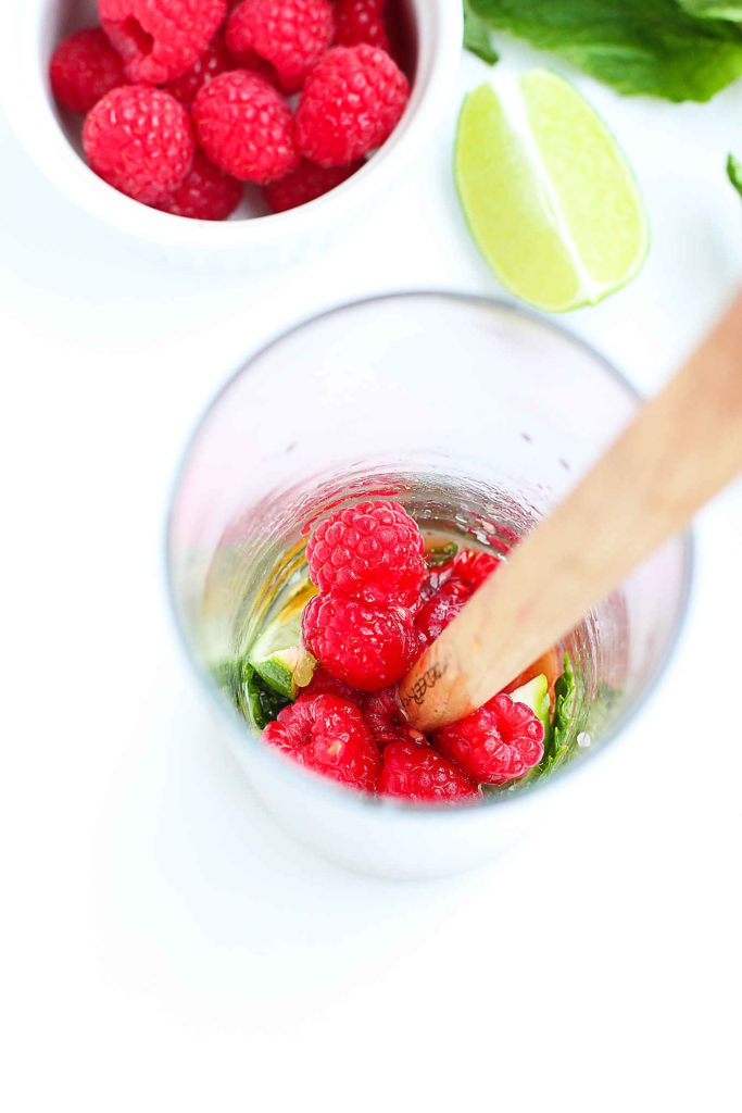 Muddling fresh raspberries, lime and mint in a glass. Mojito ingredients with a raspberry twist.