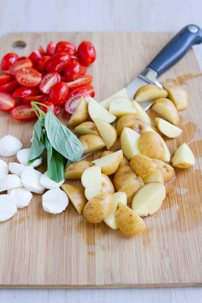 Little potatoes, bocconcini, basil and tomatoes on a wooden cutting board.