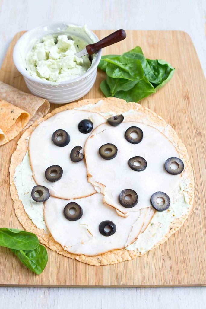 Tortillas on a cutting board, topped with cream cheese, turkey slices and black olives. #pinwheels