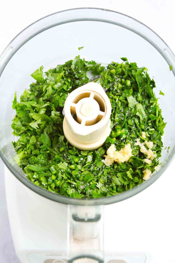 Chopped cilantro and grated garlic in the bowl of a food processor.