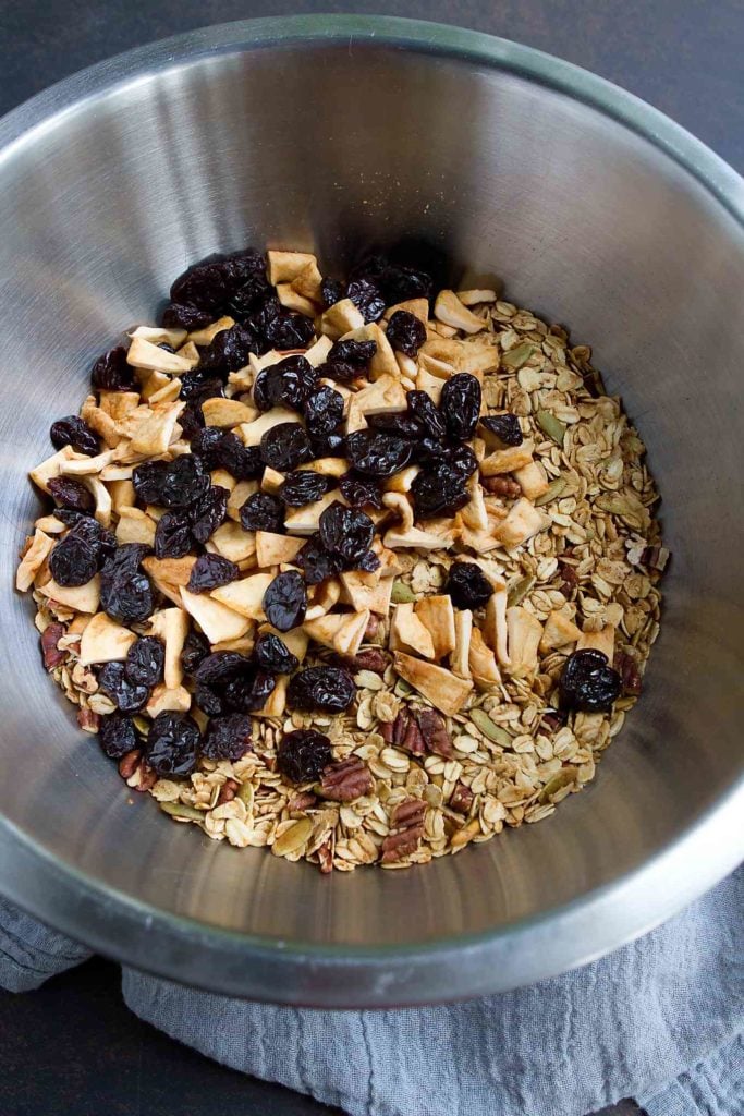 Oats, dried apples, dried cherries, pecans and pepitas in a large metal bowl.