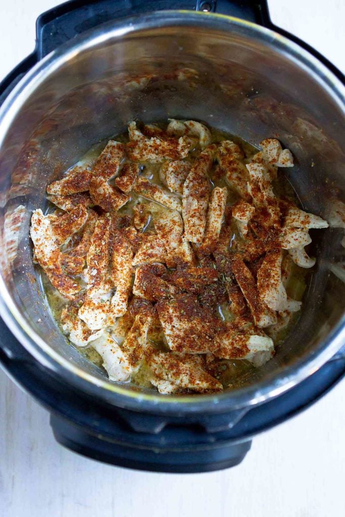 Strips of chicken breast in an Instant Pot, with spices.