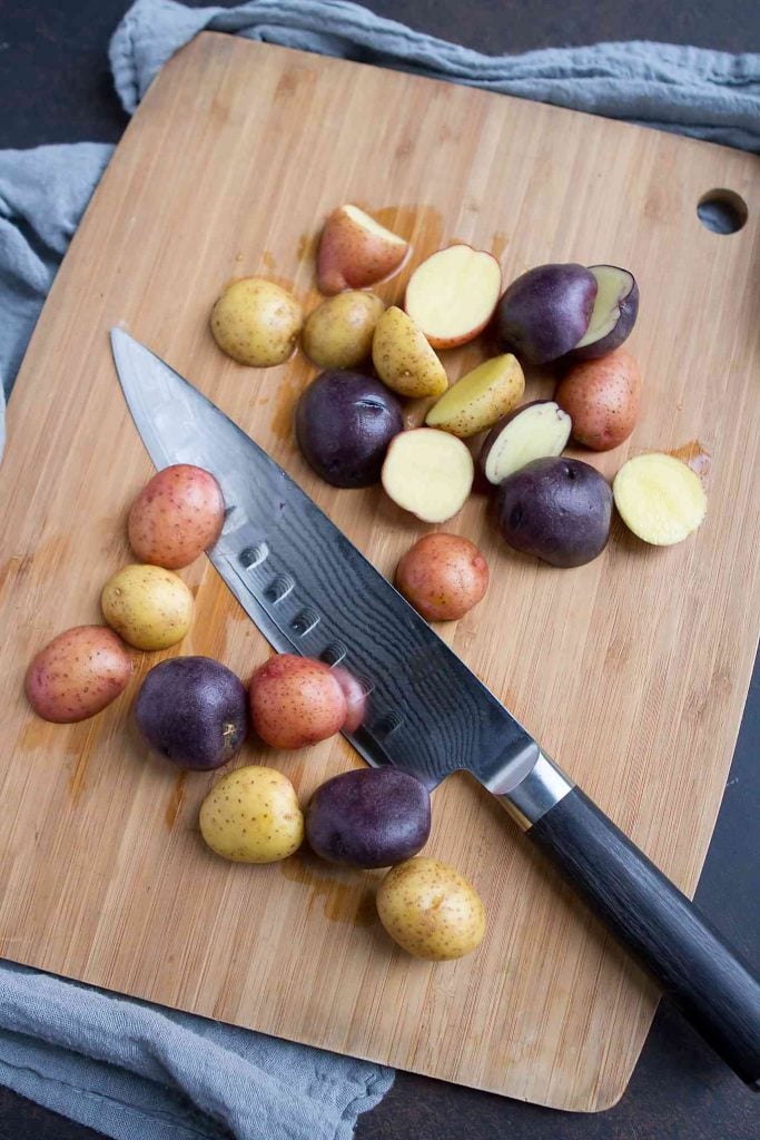 Little potatoes on a cutting board with a chef's knife.