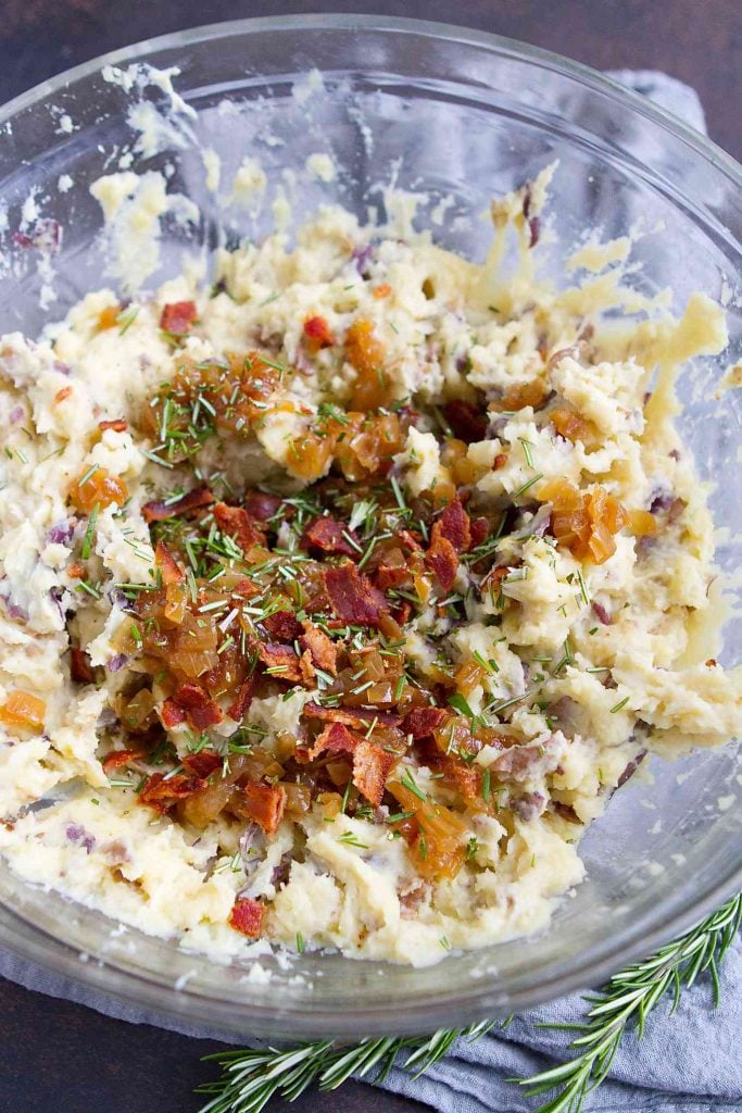 Mashed potatoes, bacon and caramelized onions in a large glass bowl.