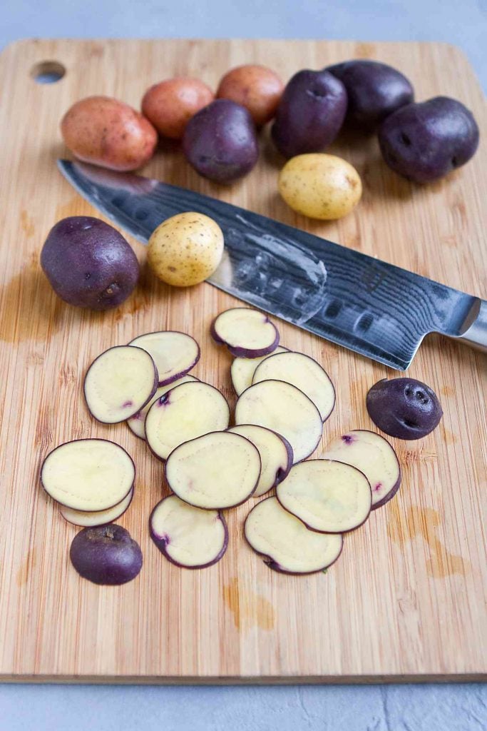 Thinly sliced potatoes and whole Little potatoes on a bamboo cutting board.