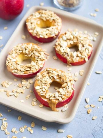 Apple slices topped with peanut and granola, on a small baking tray.
