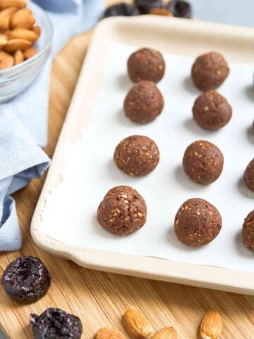 Prune almond protein balls on ceramic tray lined with parchment paper.