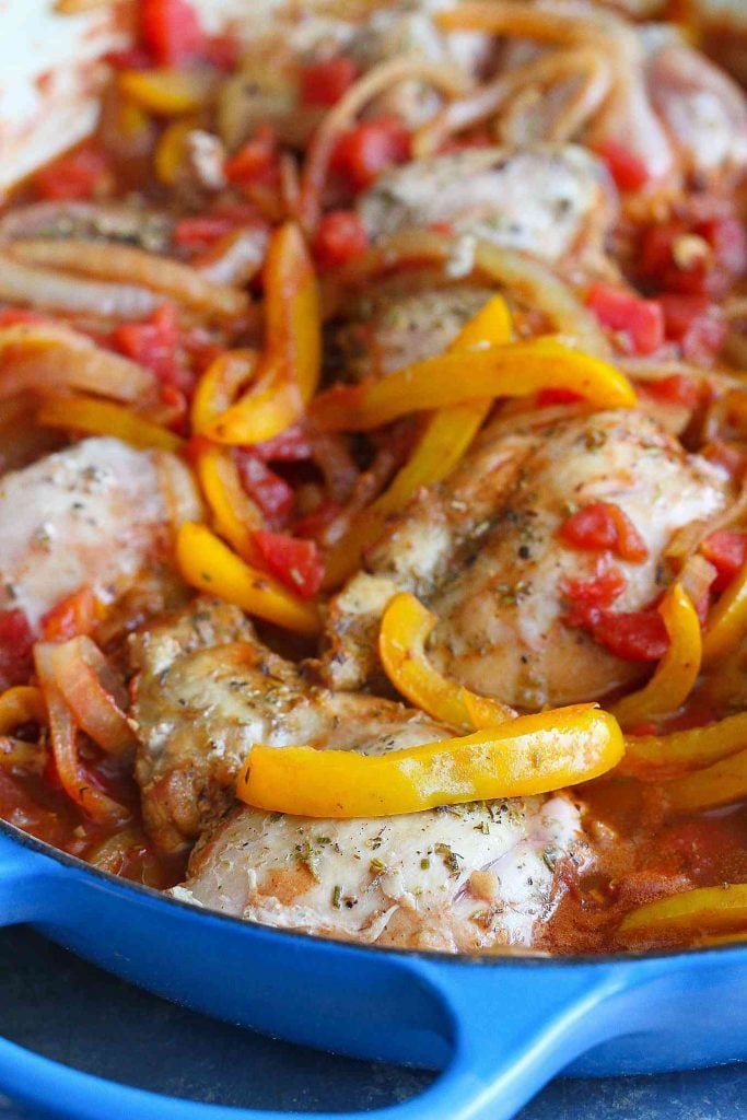 Chicken thighs simmering in a large skillet with onions and peppers