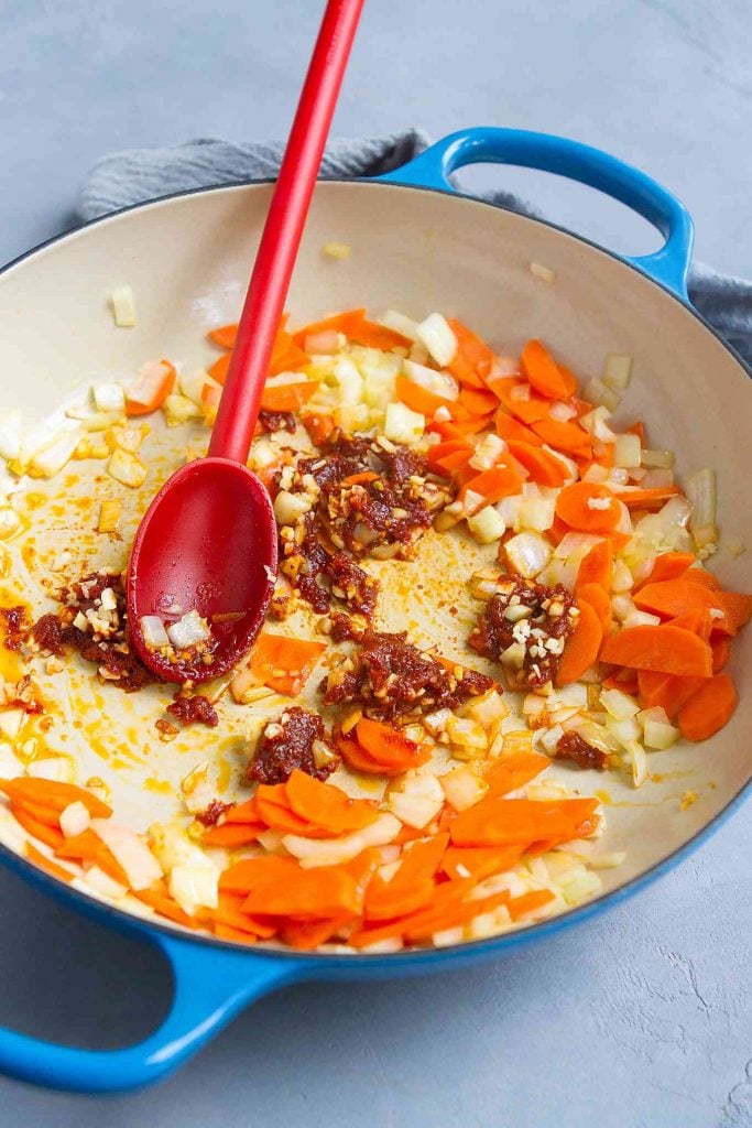 Thai red curry paste, onion, garlic, onion, carrot and ginger in a large ceramic skillet