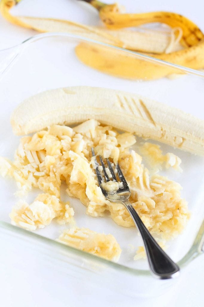 Smashing bananas with the back of a fork in a glass dish