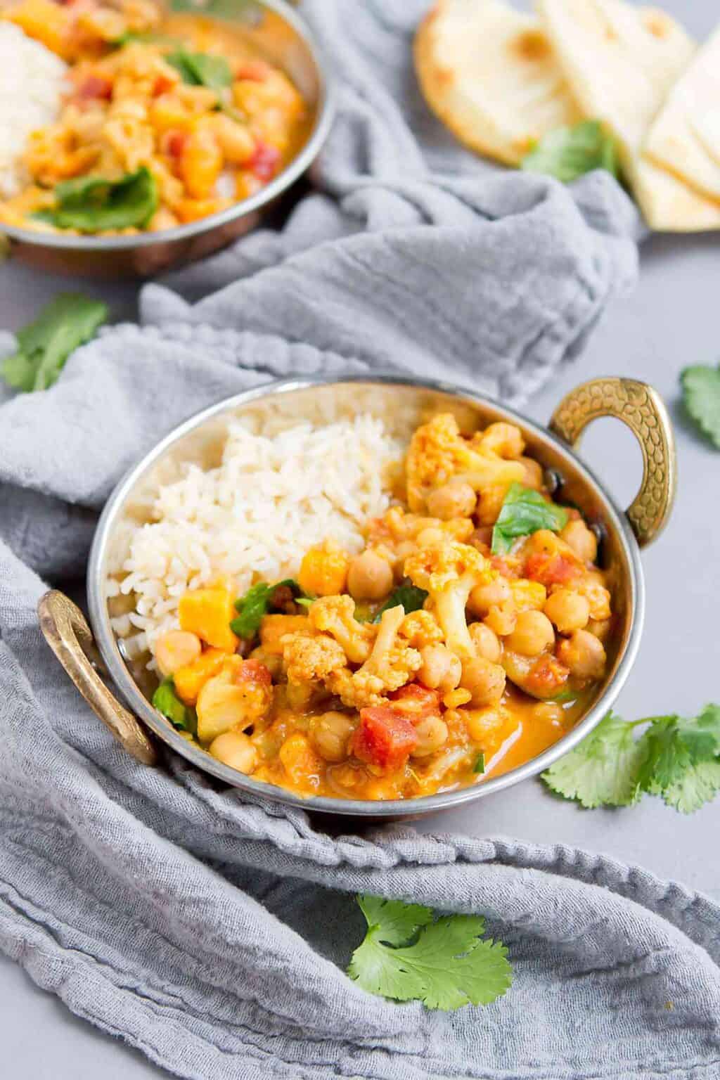 Chickpea curry and rice in brass bowls with handles, on gray napkin.