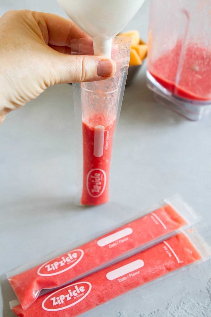 Pouring strawberry watermelon mixture through a funnel into ice pop pouch.