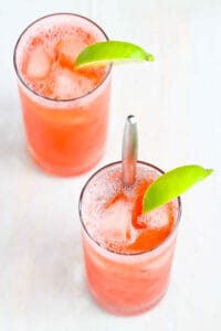 Two tall glasses filled with strawberry gin cocktail, with a lime wedge.