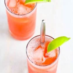 Two tall glasses filled with strawberry gin cocktail, with a lime wedge.