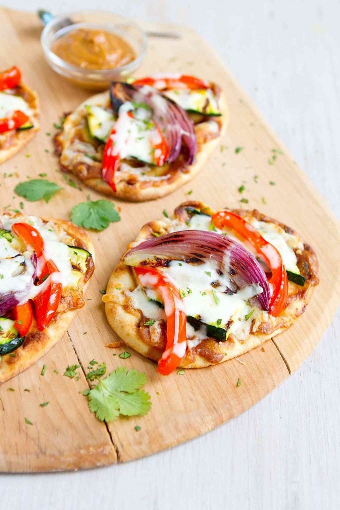 Naan bread, topped with peanut sauce, grilled vegetables and melted cheese, on a wooden pizza peel