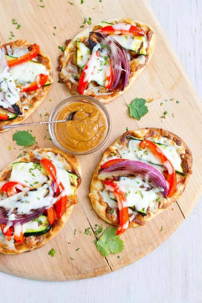 Overhead photo of Thai veggie naan bread pizzas on a pizza peel, with a bowl of peanut sauce.