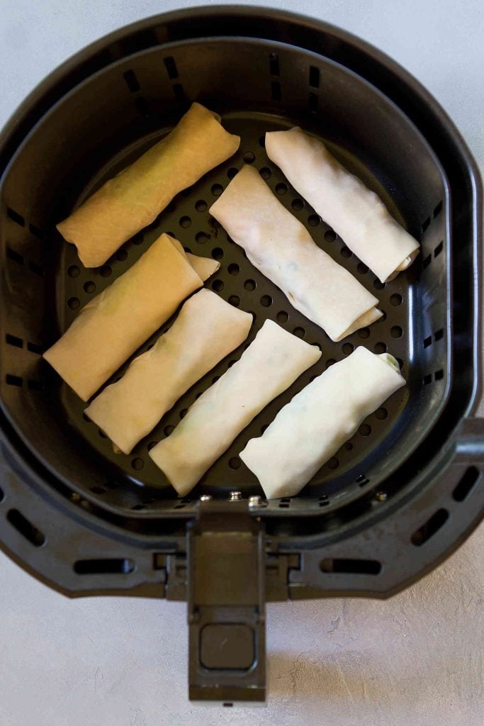 Uncooked egg rolls in the basket of an air fryer.