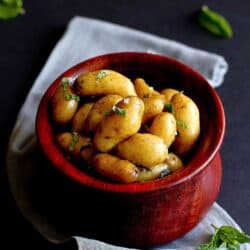 Boiled potatoes with herbs in a wooden bowl, sitting on a gray napkin.