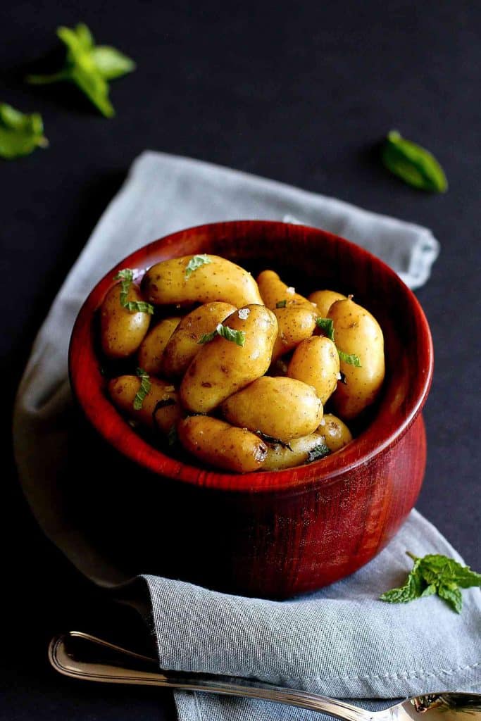 Boiled potatoes with herbs in a wooden bowl, sitting on a gray napkin.