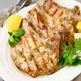 Grilled pork chops and lemon wedges on a white plate.