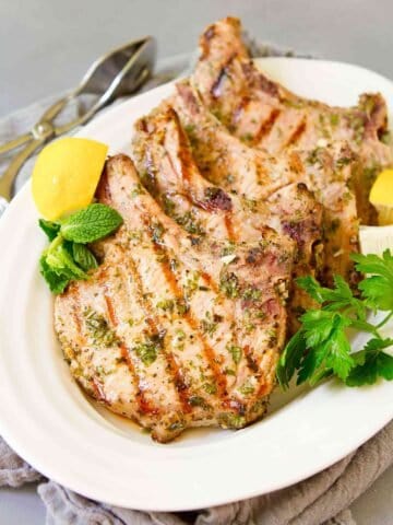Grilled pork chops and lemon wedges on a white plate.