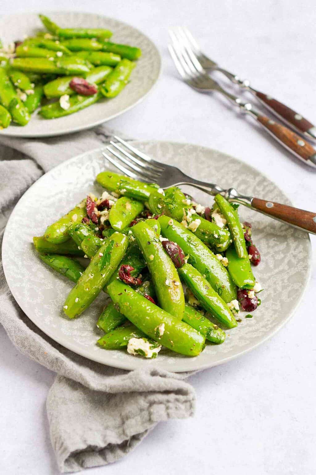 Sauteed sugar snap peas with feta and olives on two gray plates.