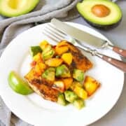 Grilled fish with avocado peach salsa on a white plate, plus two half avocados in background.