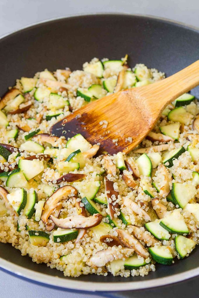 Quinoa, mushrooms and zucchini in a nonstick skillet with a wooden spoon.