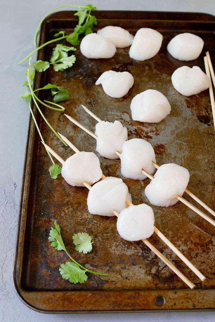 Baking sheet with scallops on skewers.
