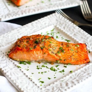 Salmon fillets with a herb glaze on white plates.