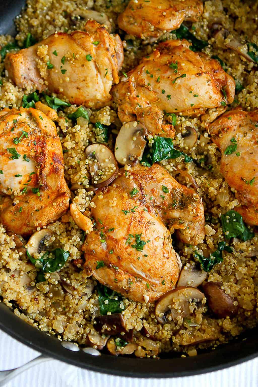 Chicken thighs, cooked quinoa, mushrooms and spinach in a black skillet.