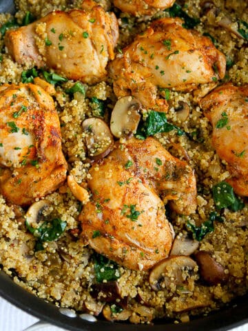 Chicken thighs, cooked quinoa, mushrooms and spinach in a black skillet.