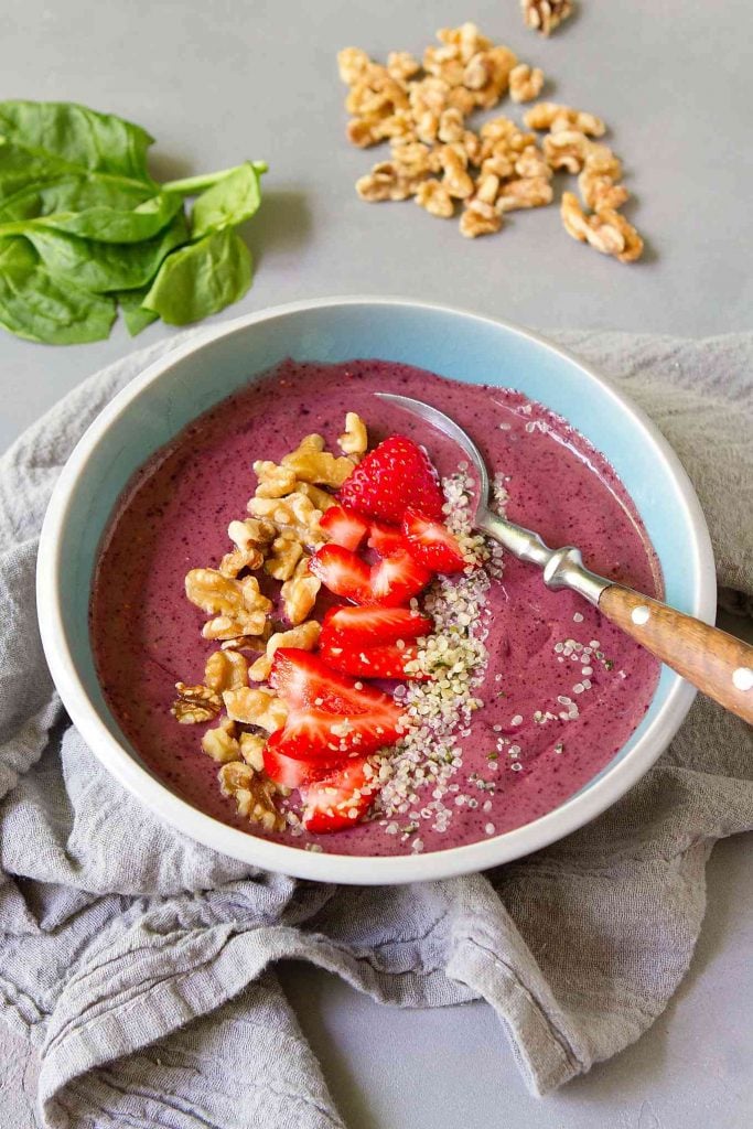 Berry smoothie bowl with nuts and fruit in a blue bowl.