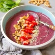 Purple smoothie bowl topped with nuts and fruit, in a blue bowl.