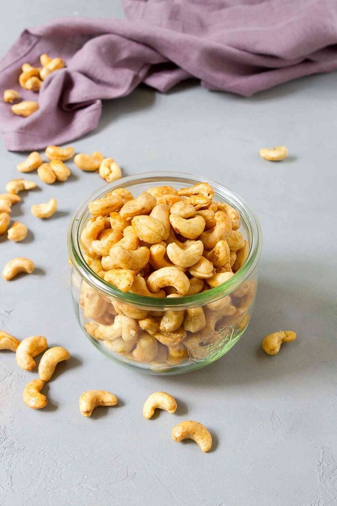 Roasted cashews, coated in maple syrup, in a glass canning jar. Cashews scattered around.