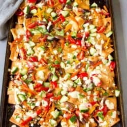 Baking sheet with nachos. With goat cheese, tomatoes, cucumber, peppers and hummus dressing.